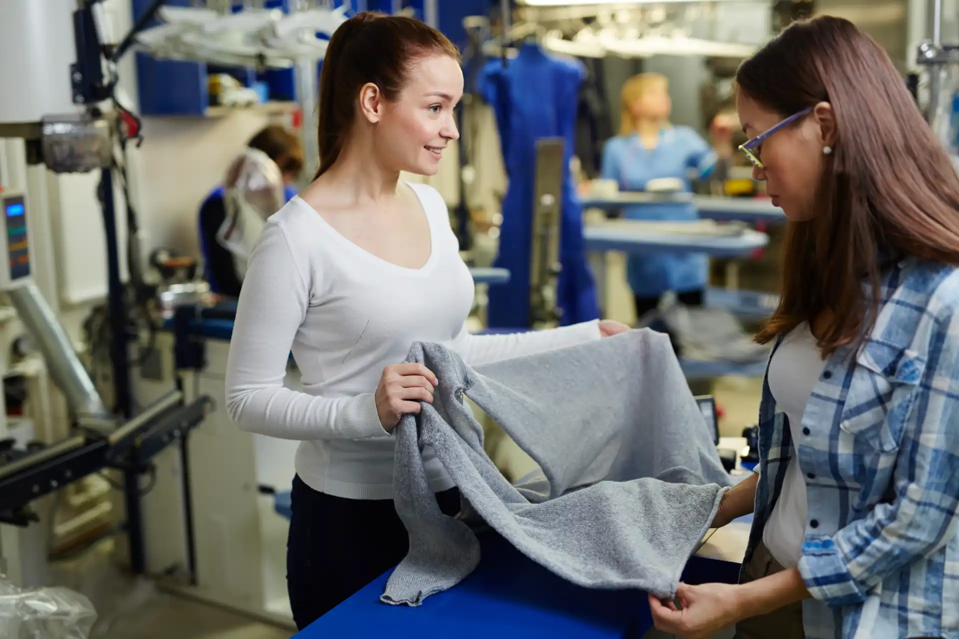Duas mulheres em uma fábrica de confecção analisando uma peça de roupa, simbolizando processos de importação têxtil e comércio internacional de materiais.